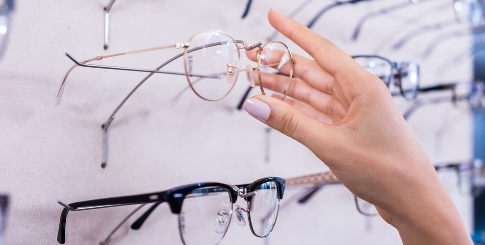 Frau greift zu großer Auswahl an Brillenfassungen an der Wand im Optikstudio